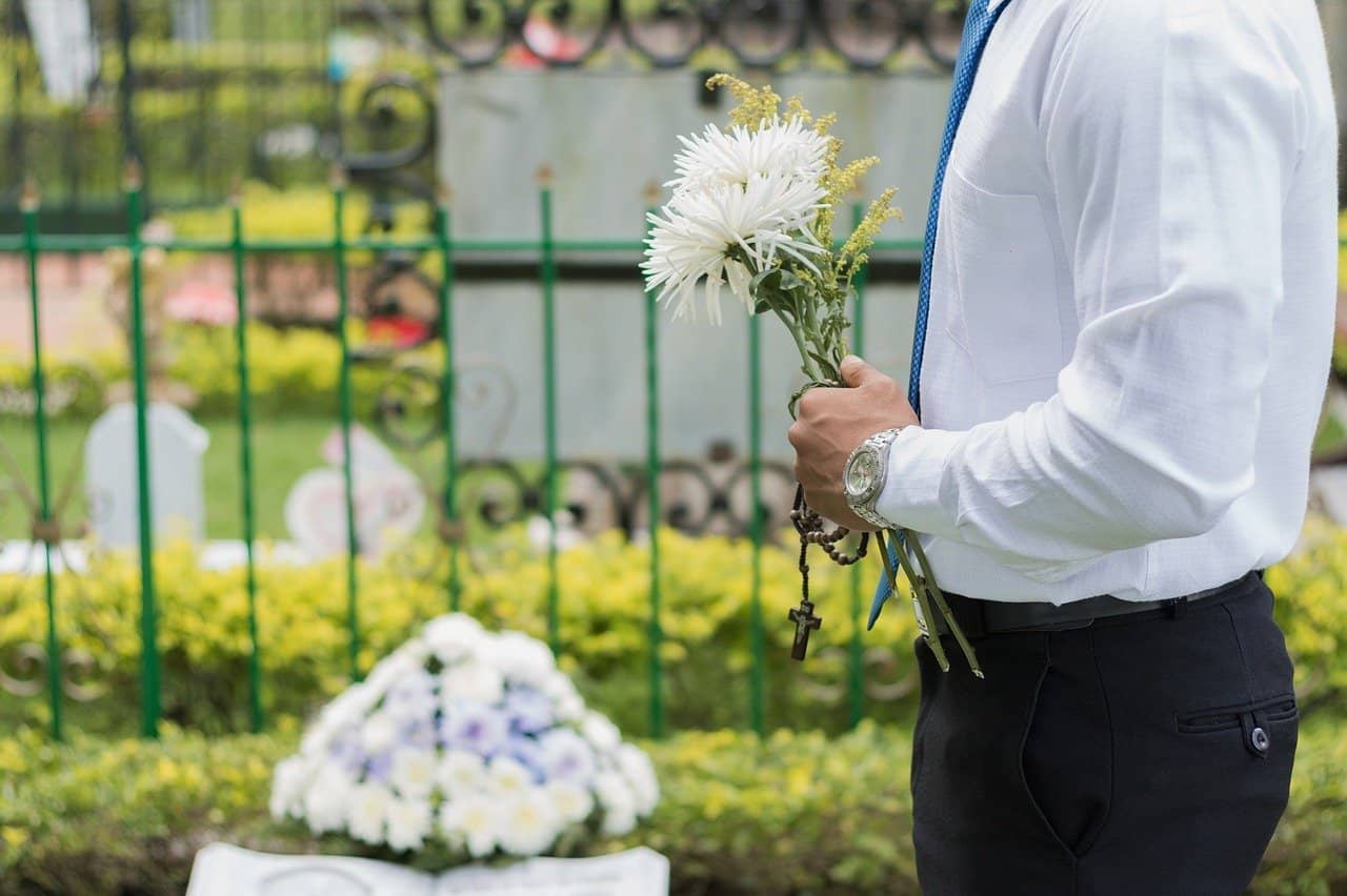 man holding flowers standing next to a grave