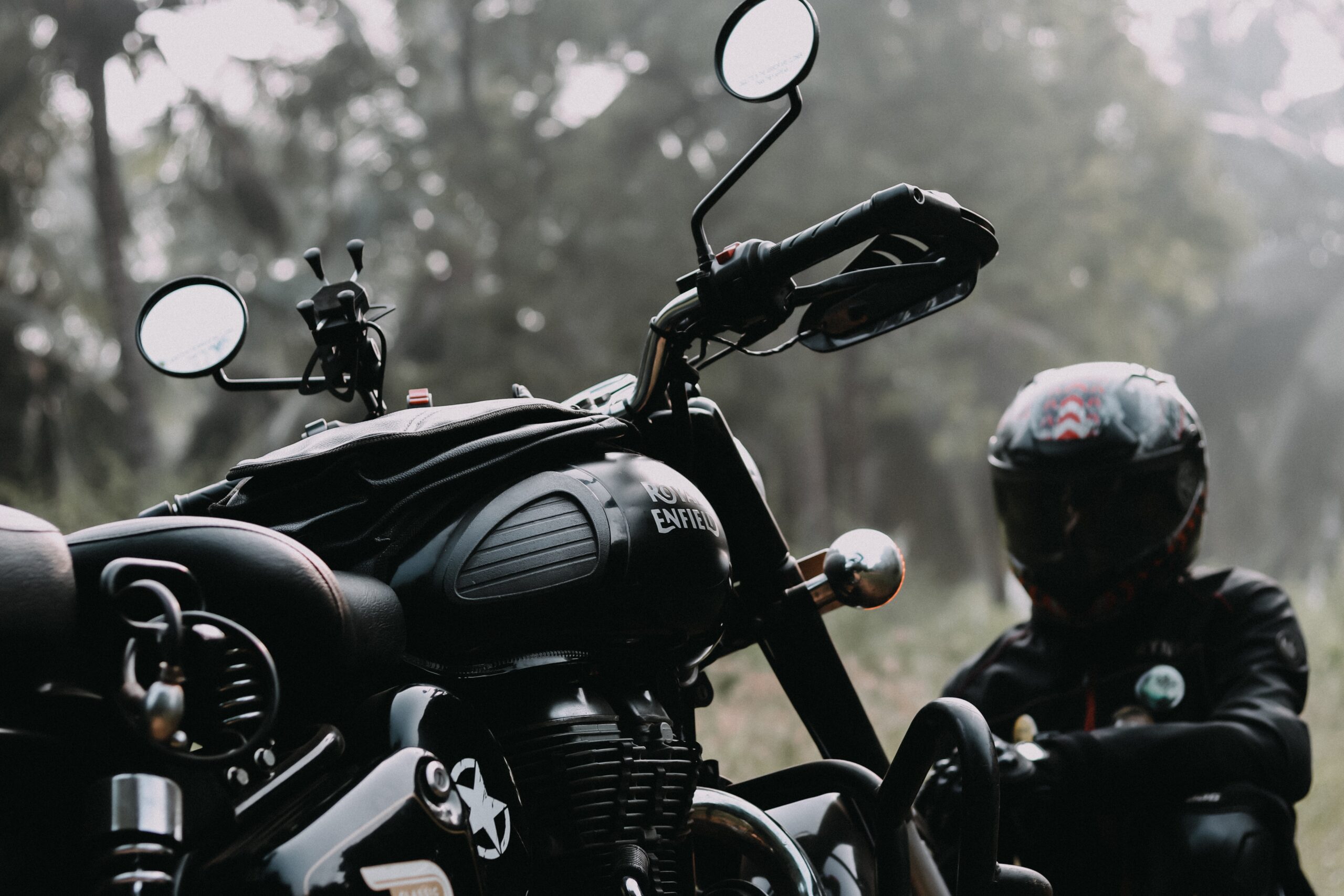 close up of black motorcycle with motorcyclist wearing black helmet in the background