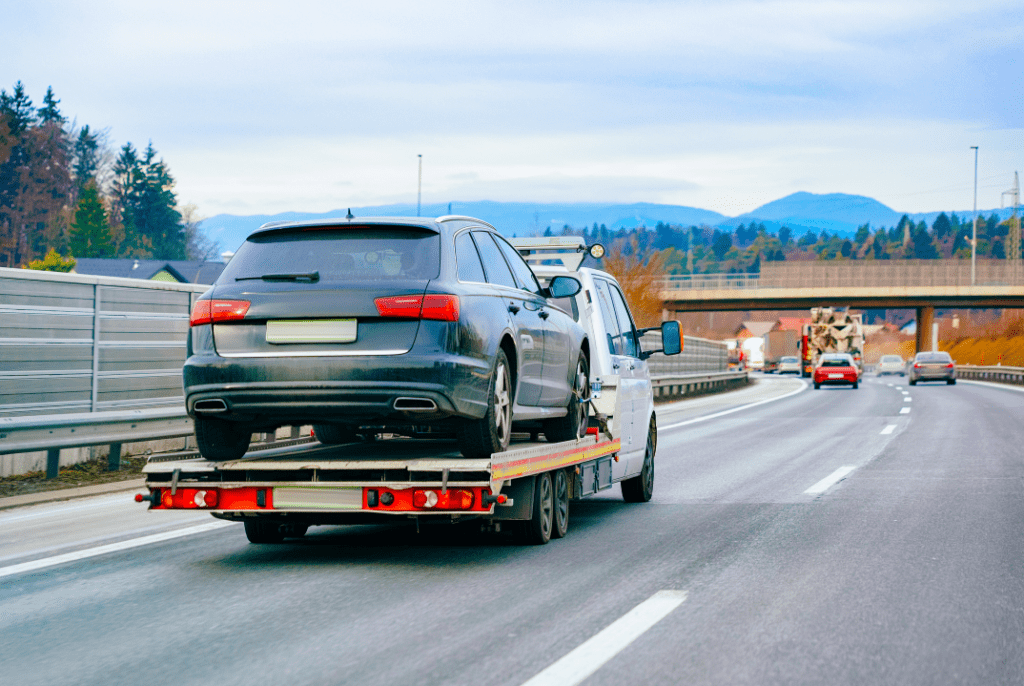 A flatbed tow truck on the road carrying a station wagon