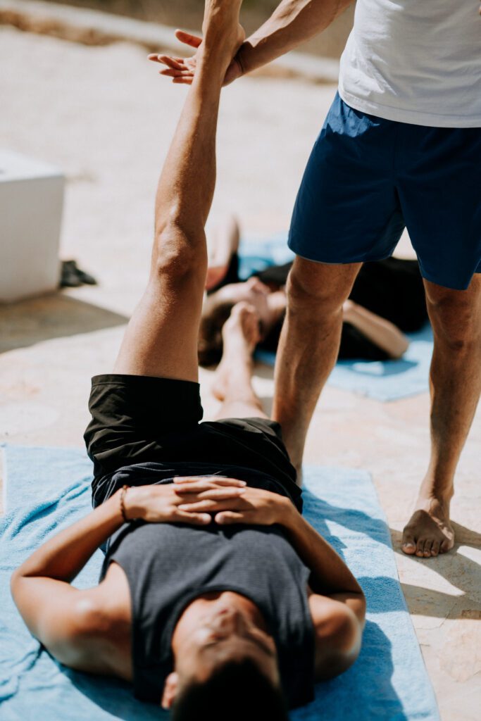 A man lying on his back while a trainer helps him stretch his leg