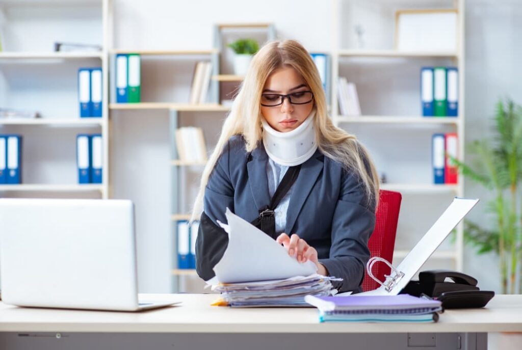 A woman with a neck and arm brace doing paperwork at her desk 