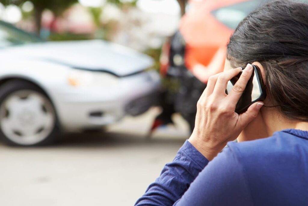 A woman makes a phone call while surveying a recent auto collision.