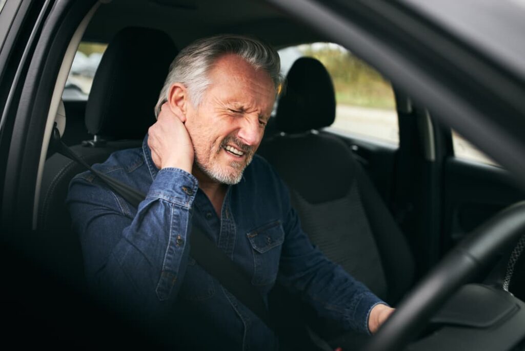 A man in his car grabs his neck in pain