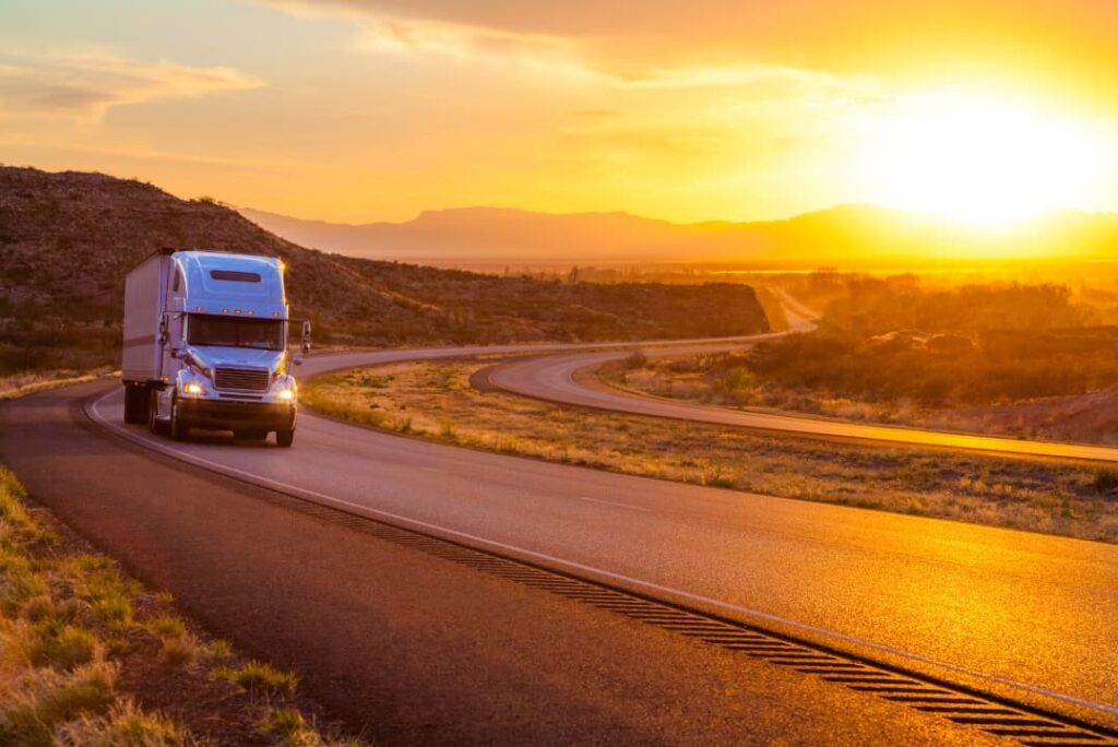 An 18-wheeler truck driving on the road with the sunset in the background