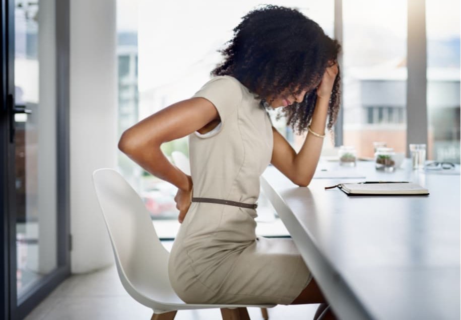 A woman feeling her back pain while sitting at her desk in the office