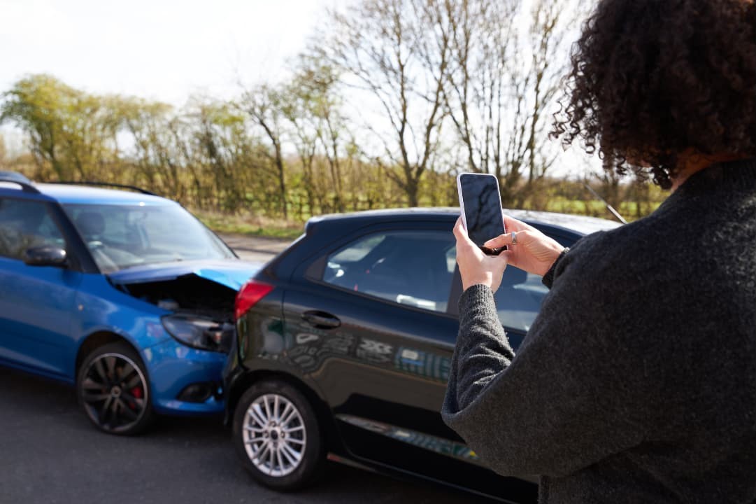 A woman documenting a car accident with a mobile phone in the middle of the road