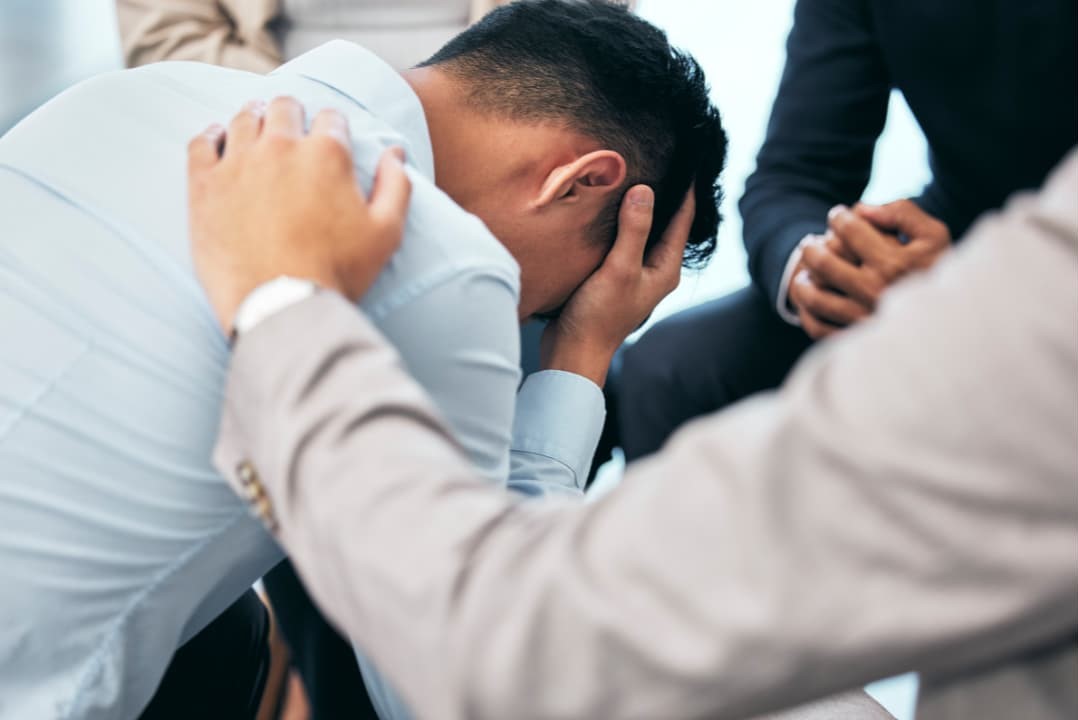 A man having an emotional distress after a wrongful death being consoled by his colleagues during work hours
