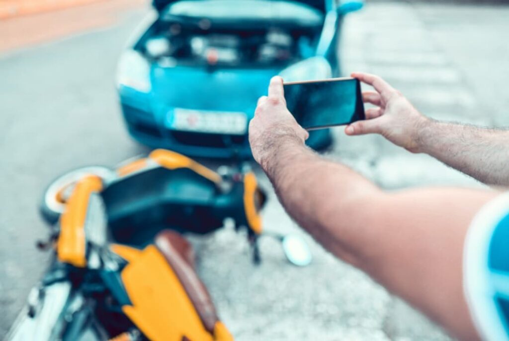 A person holding a smartphone is documenting a motorcycle accident scene.