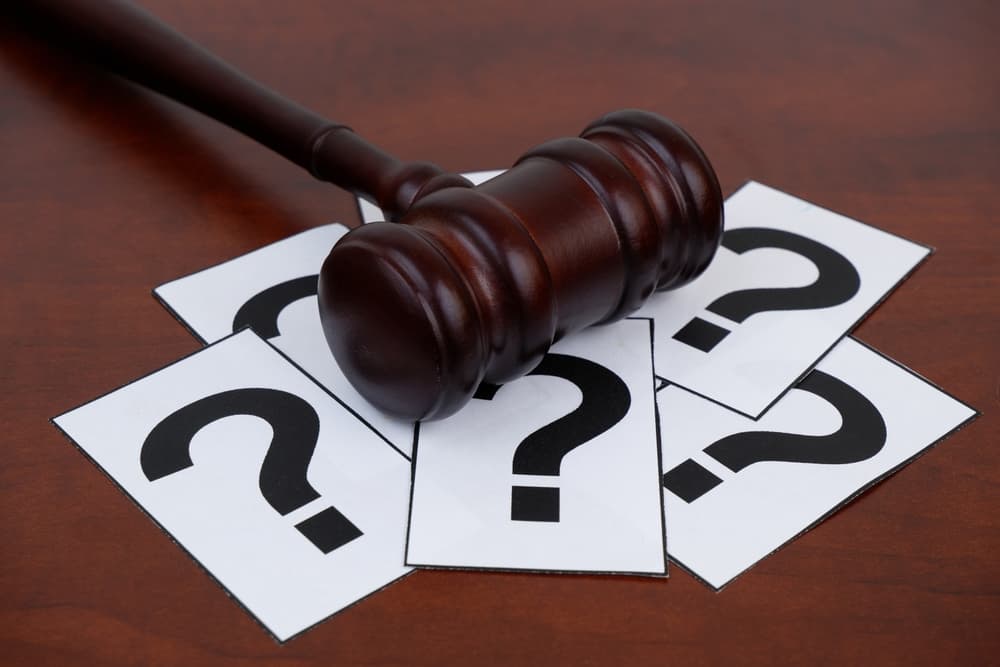 Wooden judge gavel and question marks on table.